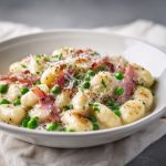Gnocchi with bacon and peas in a creamy Parmesan sauce, plated elegantly in a shallow white ceramic bowl.