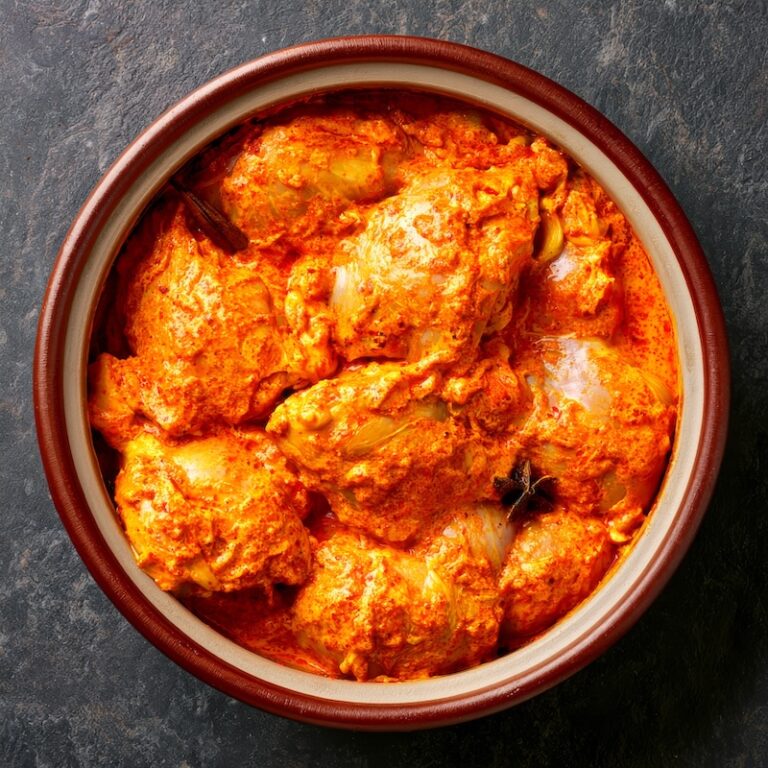 Raw chicken pieces coated in spiced yogurt marinade in a ceramic bowl