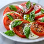 Tomato mozzarella basil salad, neatly arranged slices of ripe red tomatoes and fresh mozzarella, whole basil leaves