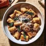 A bowl of rigatoni in chicken liver sauce, crisped sage leaves scattered visibly on top