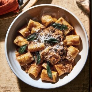 A bowl of rigatoni in chicken liver sauce, crisped sage leaves scattered visibly on top