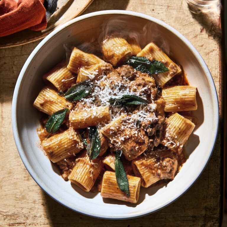 A bowl of rigatoni in chicken liver sauce, crisped sage leaves scattered visibly on top
