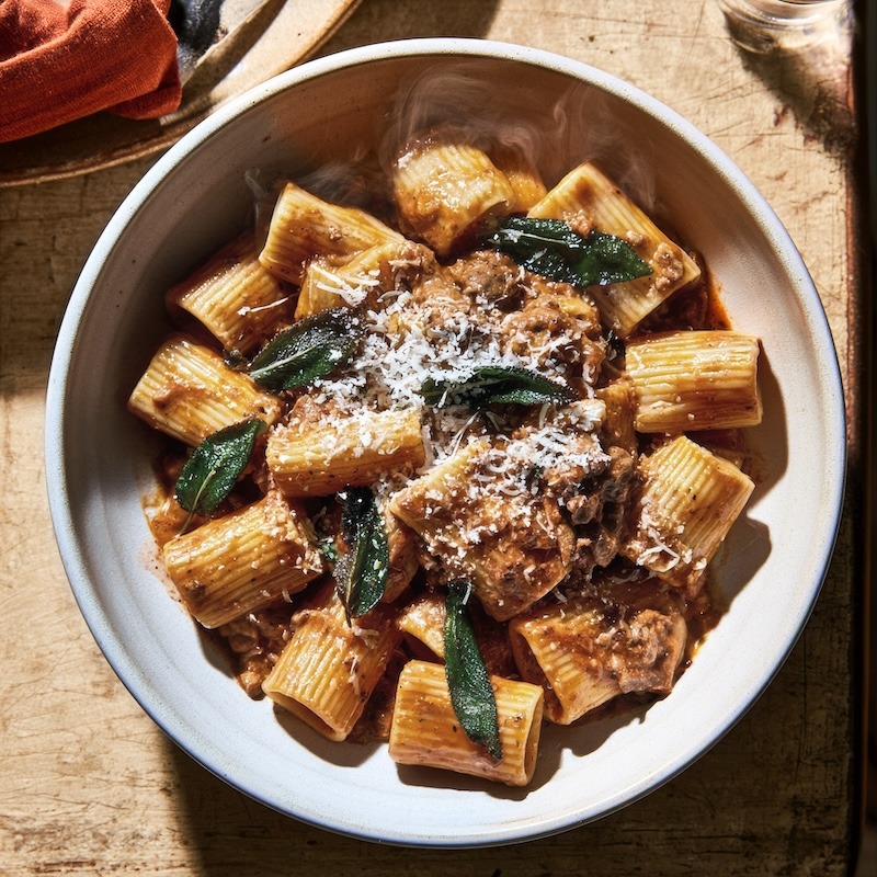 A bowl of rigatoni in chicken liver sauce, crisped sage leaves scattered visibly on top