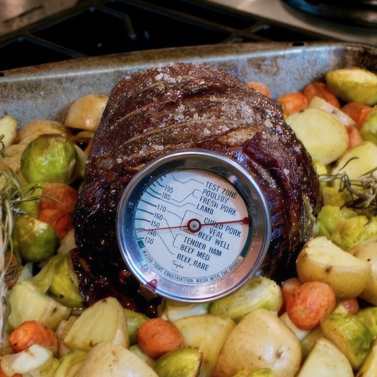 A beef roast, a meat thermometer, and potatoes in a roasting pan.