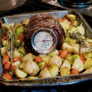 A beef roast, a meat thermometer, and potatoes in a roasting pan.