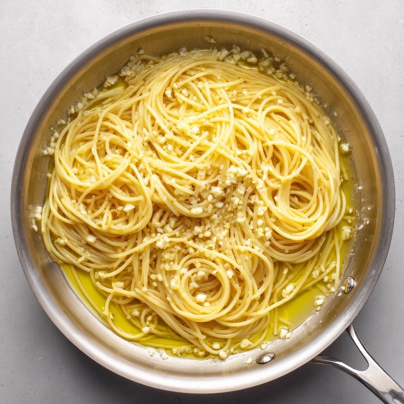 Spaghetti added to the pan of minced garlic and virgin olive oil.