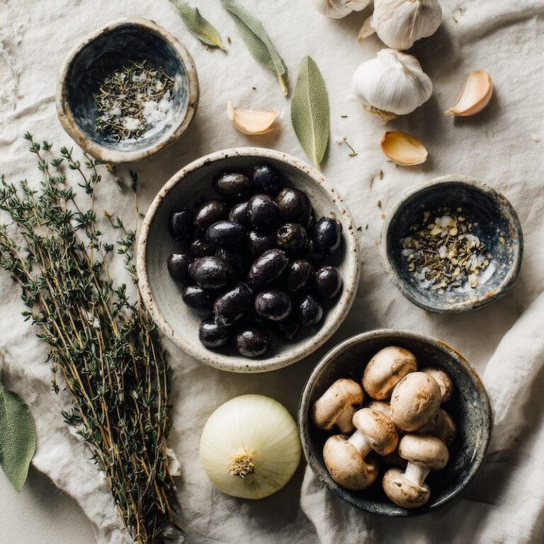 Whole Nicois olives, a bundle of fresh thyme, dried sage and basil in small ceramic bowls