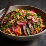A wide bowl of Korean beef stir fry over rice noodles