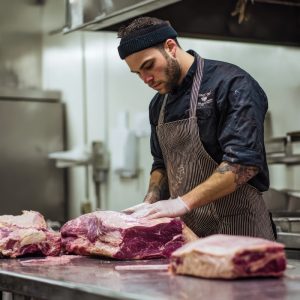 A professional butcher fabricates a side of beef on a steel table.