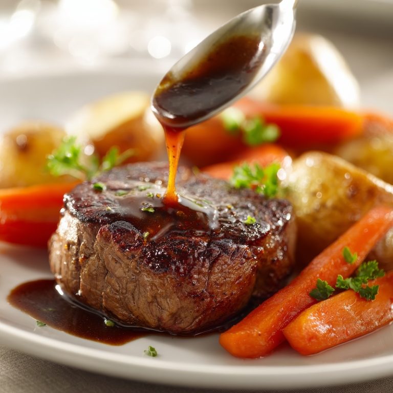 A perfectly cooked filet mignon steak on a white plate, served with glossy demi-glace