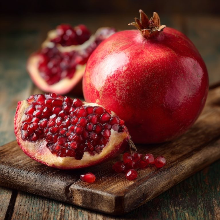 Vibrant whole pomegranate on a rustic wooden cutting board.