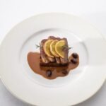 A white plate with seared duck topped with Bigarade Sauce