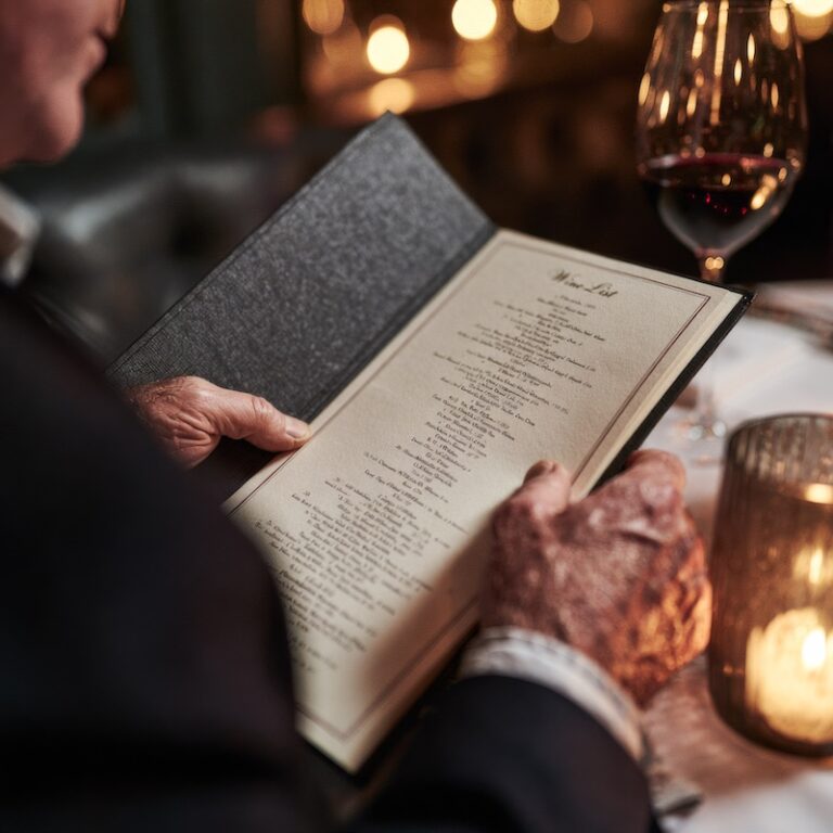 hands reviewing a wine list menu at a restaurant table