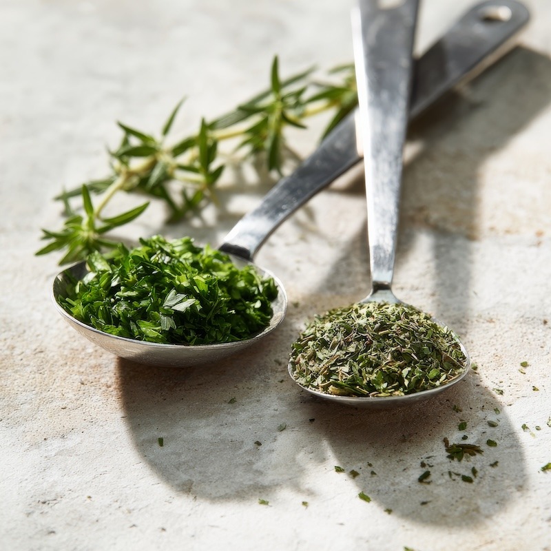 A tablespoon of fresh chopped herbs next to a teaspoon of dried herbs demonstrating herb conversion ratios.