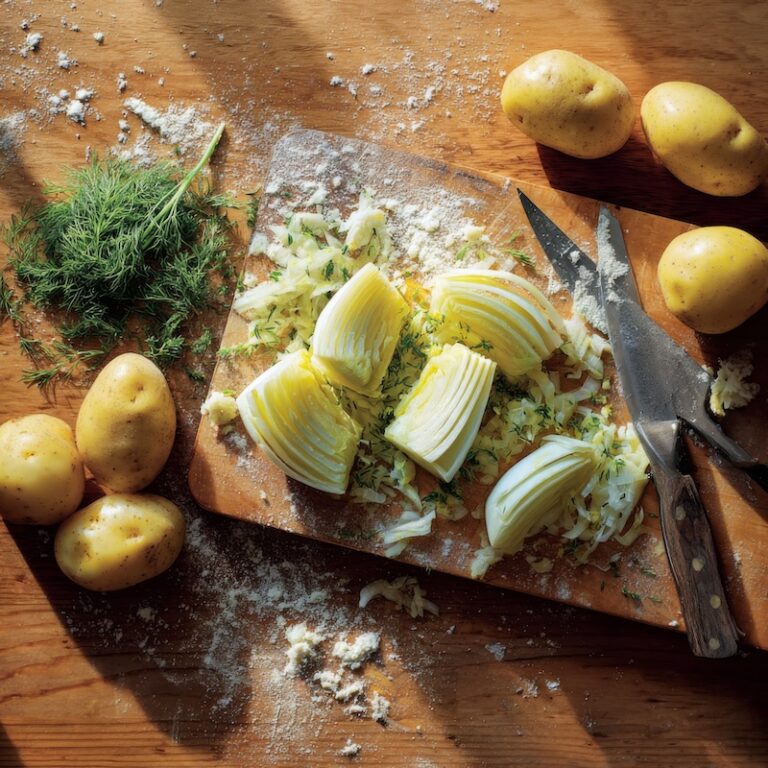 Sliced fennel bulbs beside Yukon Gold potatoes on a wooden cutting board