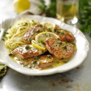 A white plate with veal francaise and a side of pasta