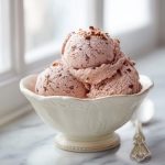 Strawberry chocolate gelato made with minced almonds scooped into a chilled ceramic bowl.