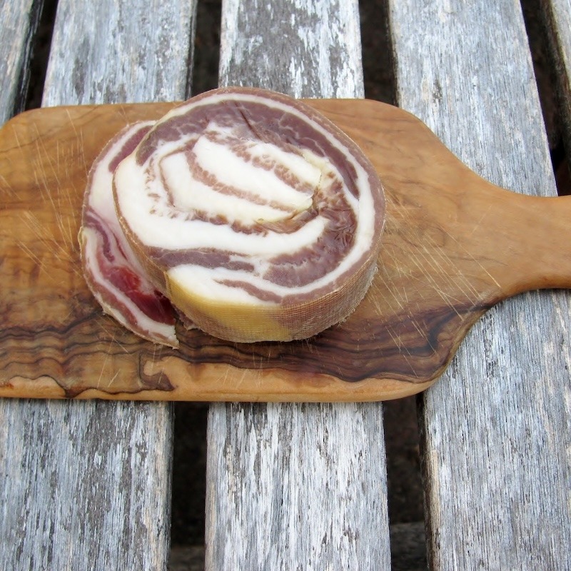 A slice of Italian cured pancetta on a cutting board.