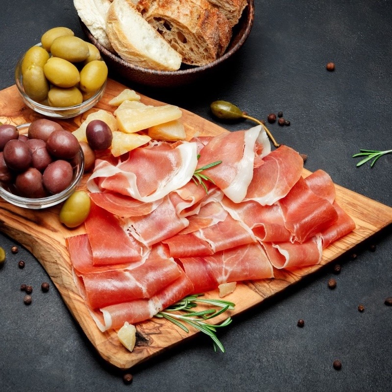 Slices of just sliced prosciutto on board with olives