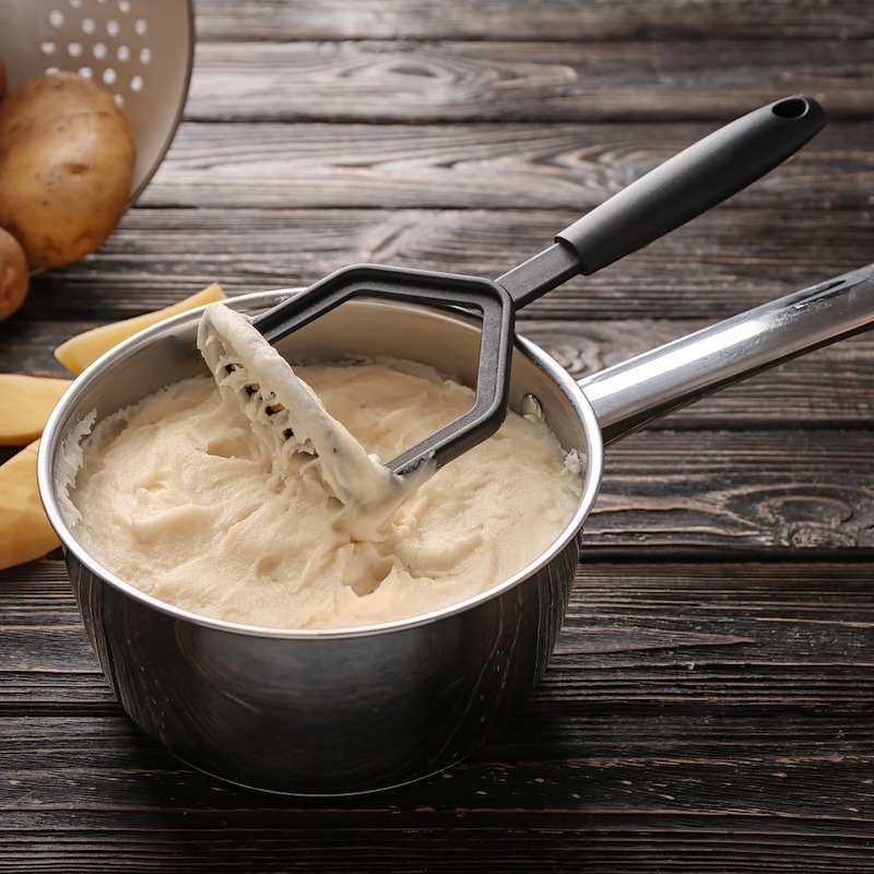A pot of mashed potatoes with a potato masher.