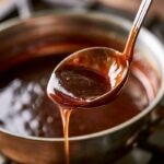 A ladle lifting glossy, deep-brown demi-glace from a saucepan
