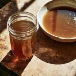 a mason jar of dark, glossy brown veal stock next to a shallow bowl of the same stock cooling