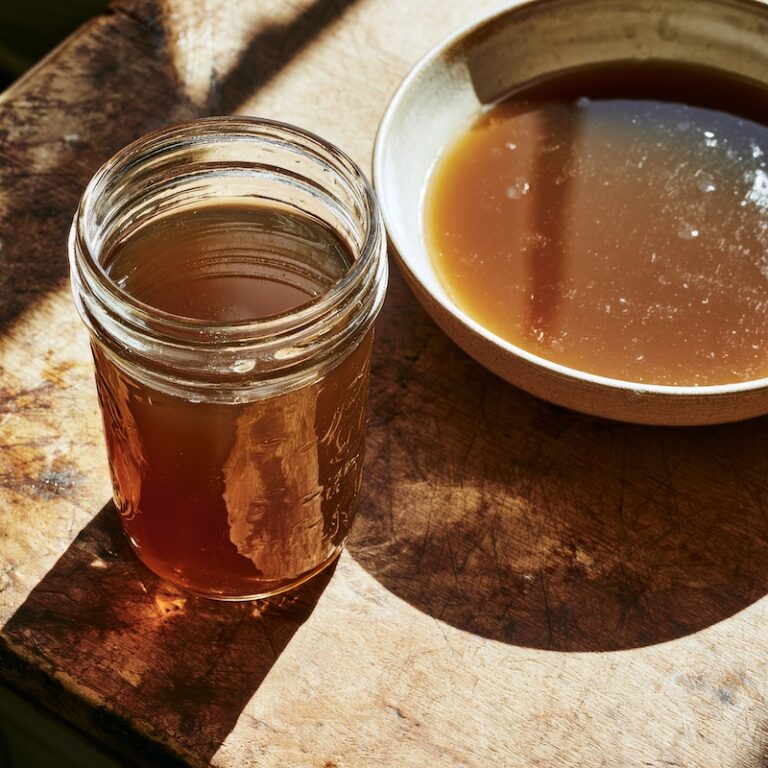 a mason jar of dark, glossy brown veal stock next to a shallow bowl of the same stock cooling