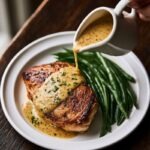 Mustard white wine sauce in a small white ceramic pitcher being poured over a pan-seared chicken breast