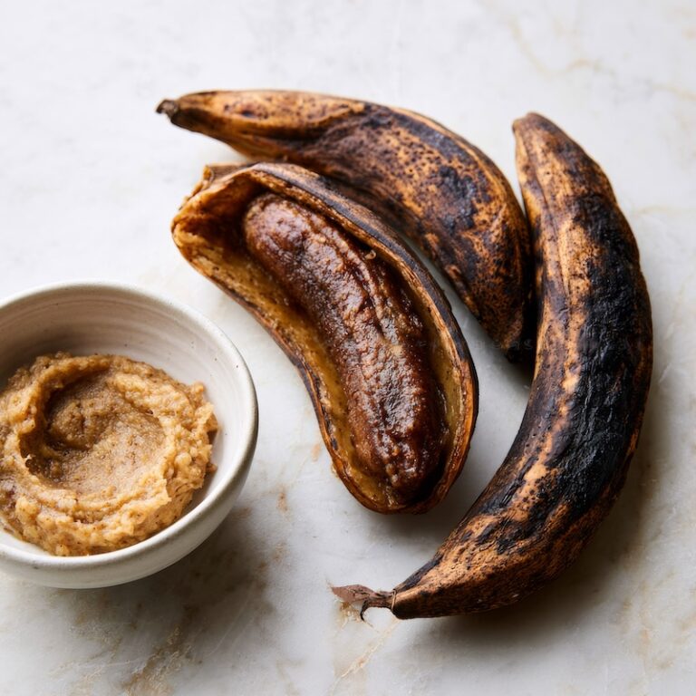 Three almost-black overripe bananas on a pale marble surface
