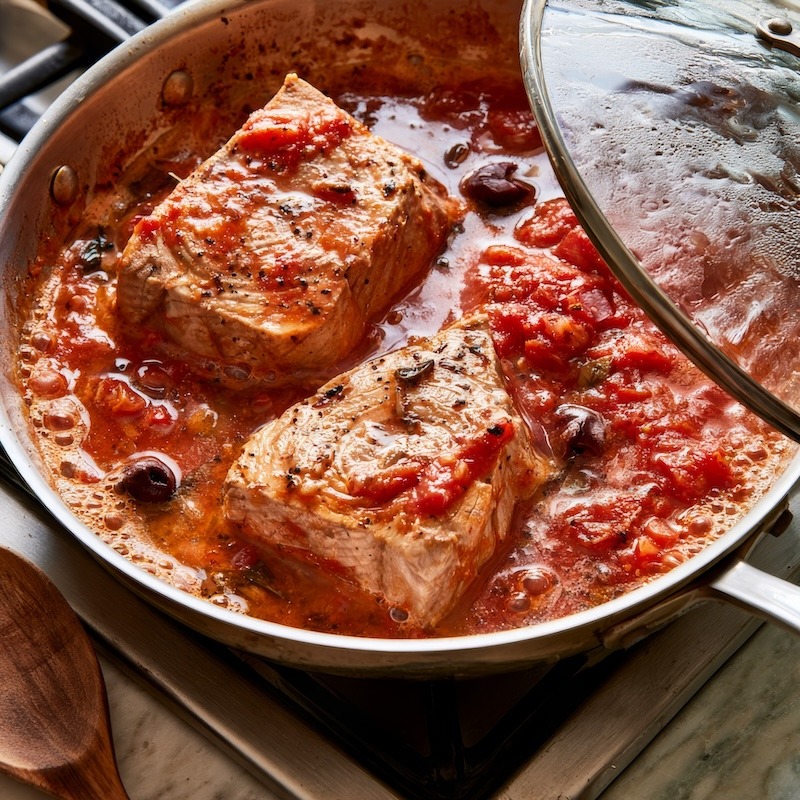 Two tuna pieces nestled in gently simmering marinara in a small skillet