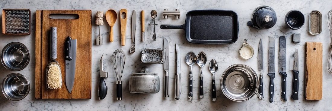 collection of kitchen tools arranged with intention: chef’s knife, paring knife, wooden spoons, whisk, tongs, cutting board, cast iron skillet, stainless steel pans, microplane, measuring cups, stand mixer, blender, food processor